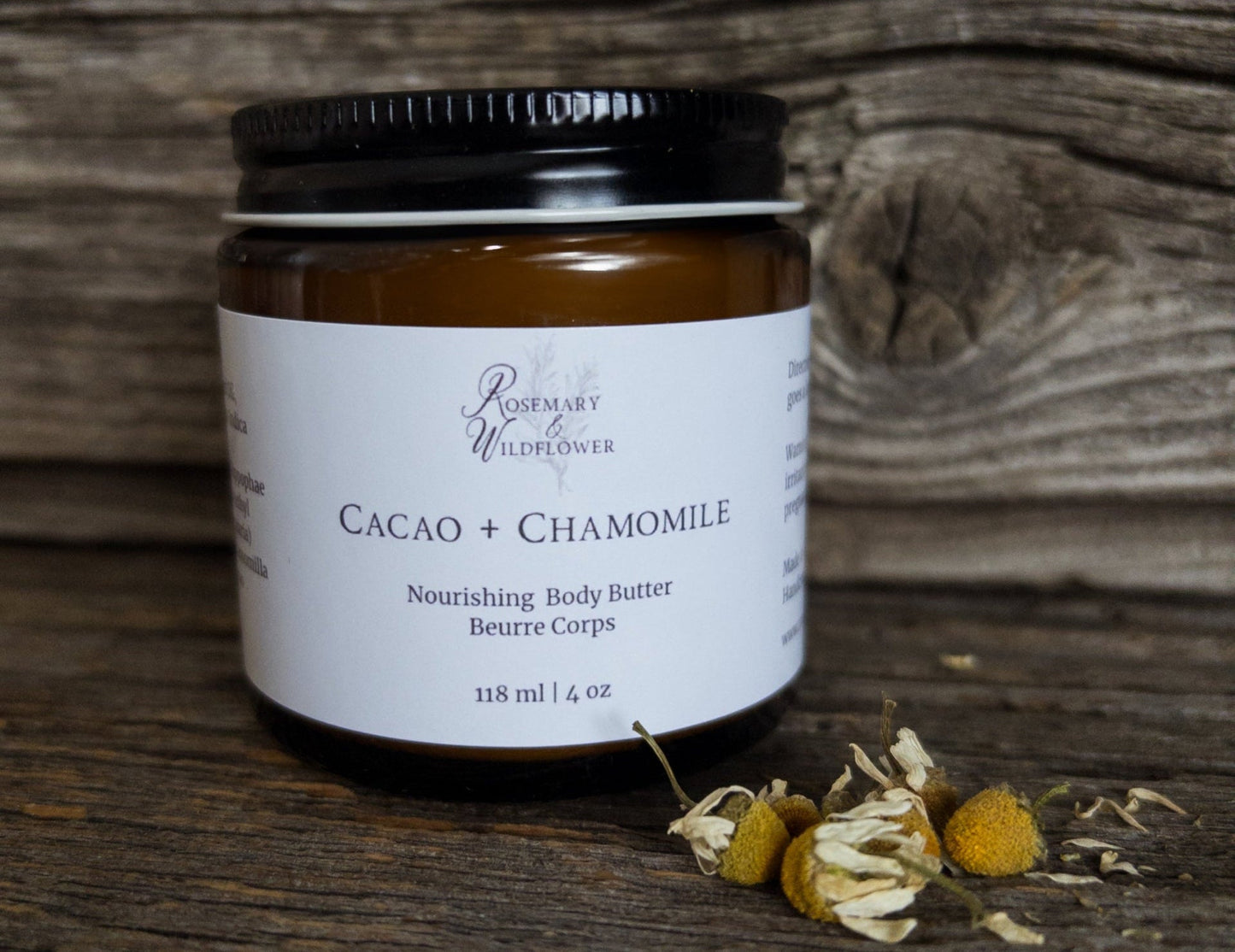 Cacao + Chamomile body butter jar with dried chamomile flowers on a wooden surface.