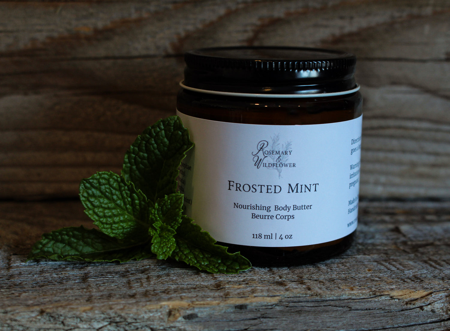 Jar of Frosted Mint body butter with a mint leaf on a wooden surface