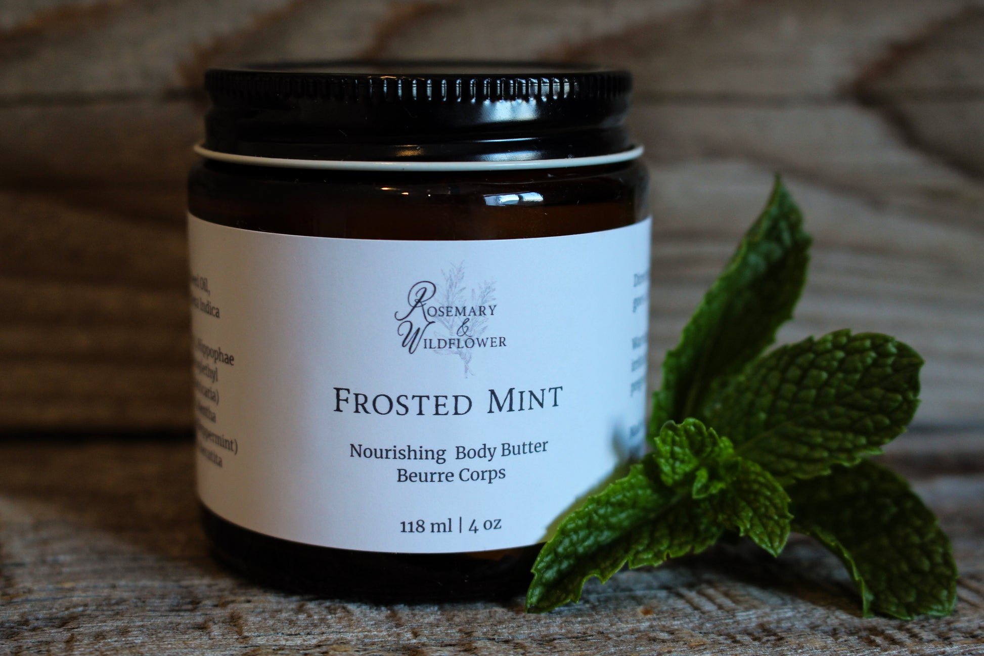 Jar of Frosted Mint body butter with a sprig of mint on a wooden surface